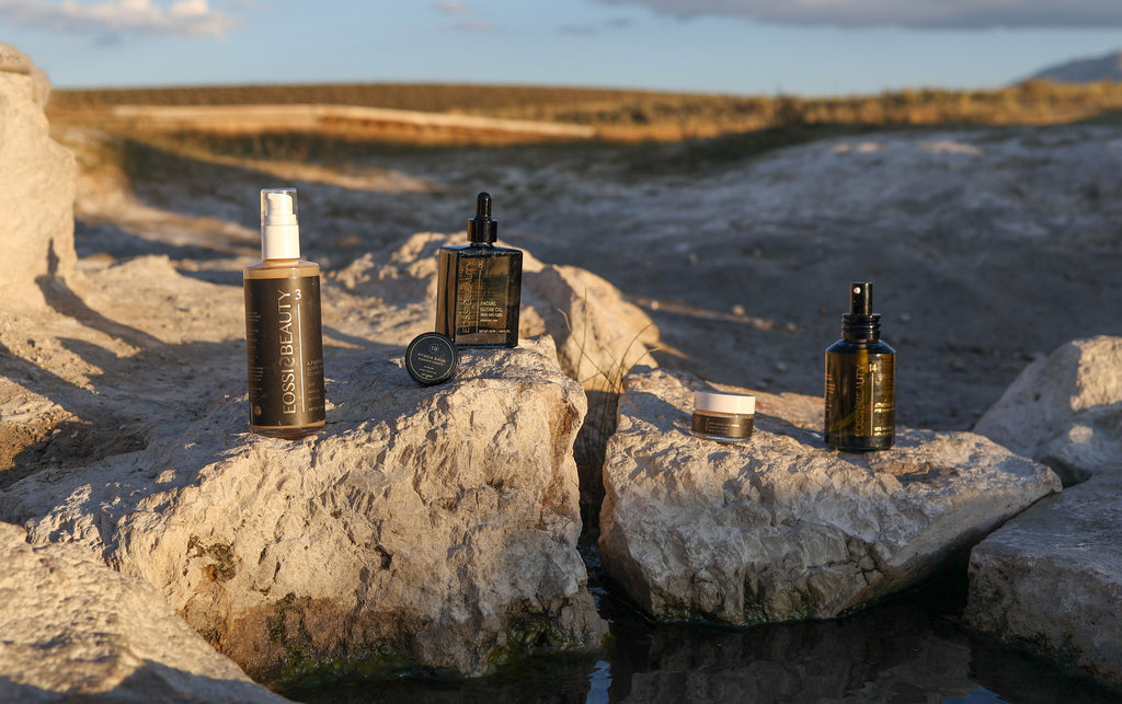 A selection of Eossi Beauty skincare products including oils, serums and creams arranged on a rugged rock outdoors, highlighting natural ingredients.