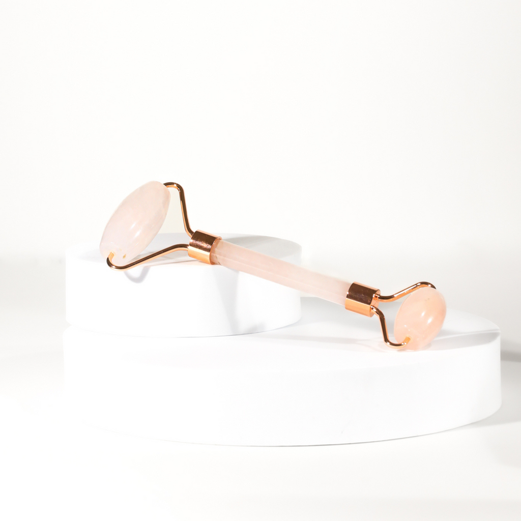 Rose quartz facial roller with copper handle displayed on a white cylindrical pedestal, showcasing its elegant design for beauty routines.